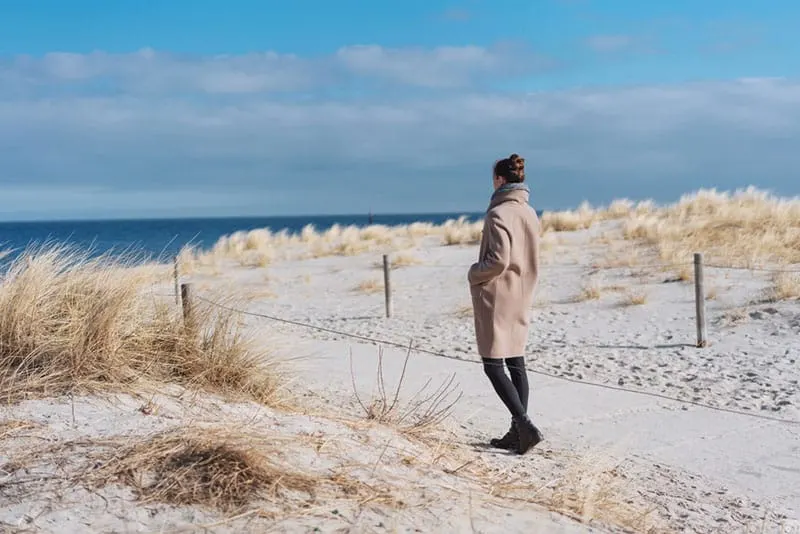 woman in coat walking on the beach