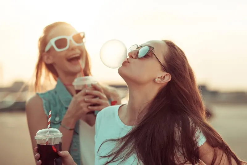 woman making balloon from chewing gum while her friend laughing