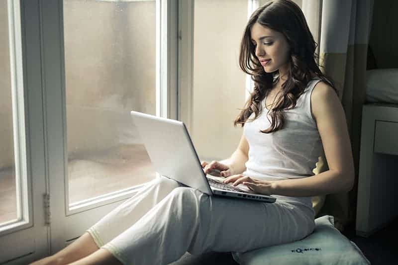 donna che scrive sul suo portatile accanto alla finestra
