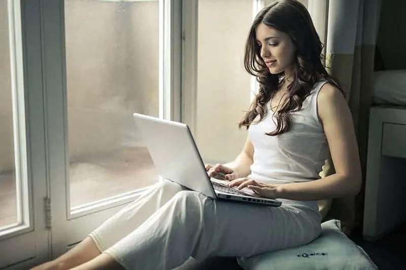 woman typing on her laptop beside window