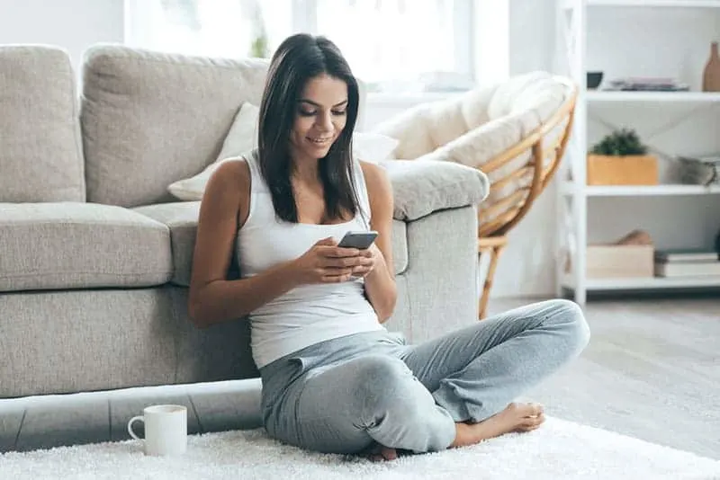woman typing on her phone while sitting on floor