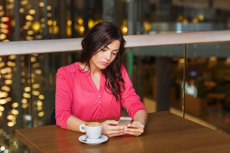 donna con smartphone e caffè al ristorante
