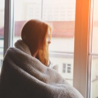 a sad girl wrapped in a blanket looks out the window