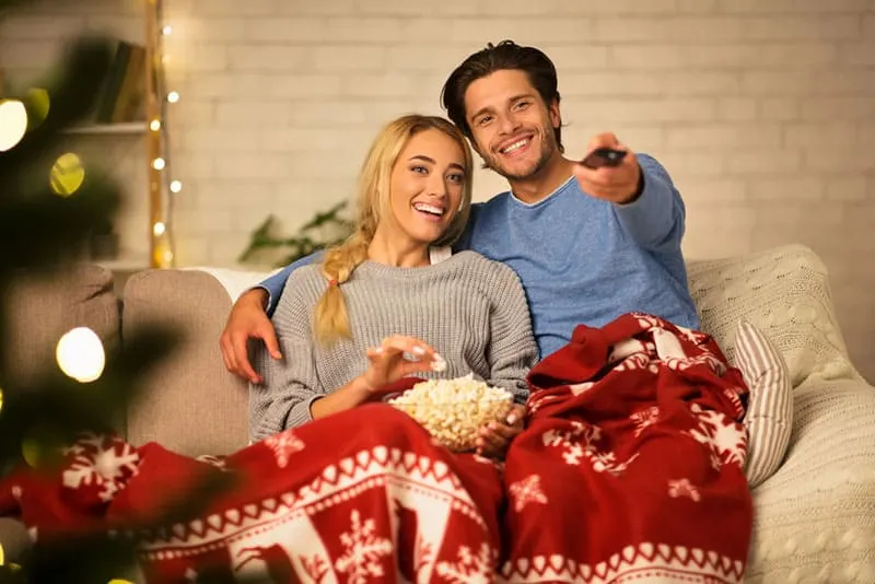Loving couple watching tv and eating popcorn at home, covered with blanket