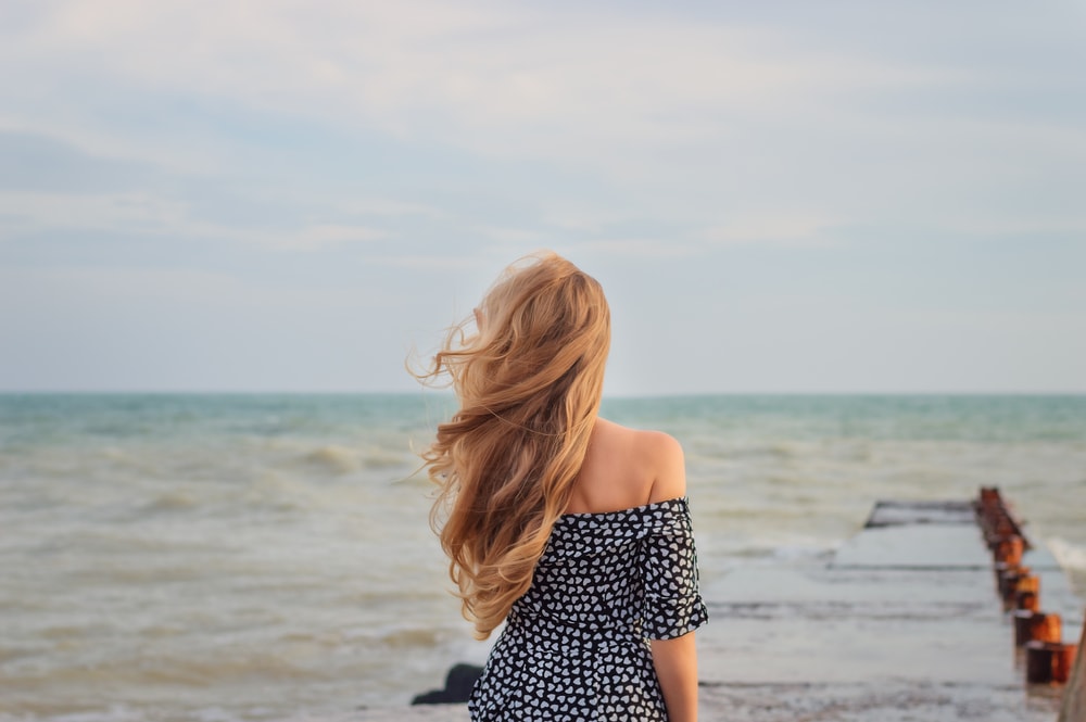 a beautiful blonde stands on the dock and watches the sea