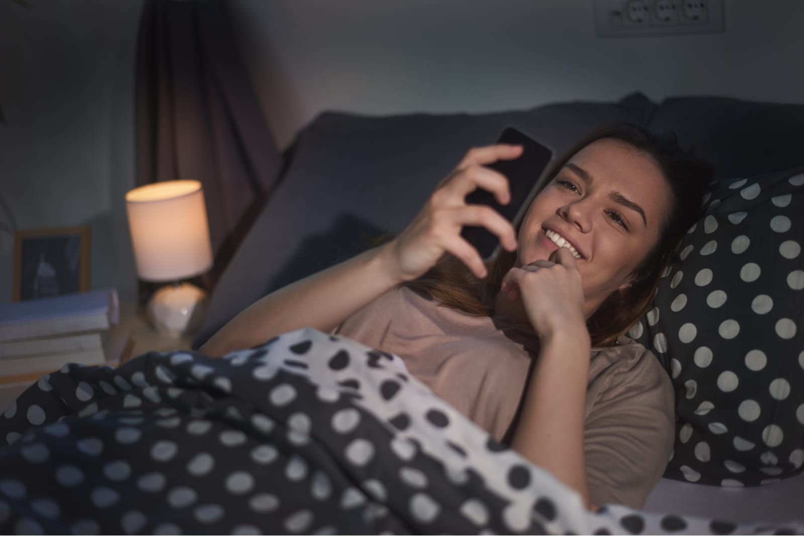 una ragazza felice la sera si sdraia a letto e usa il cellulare