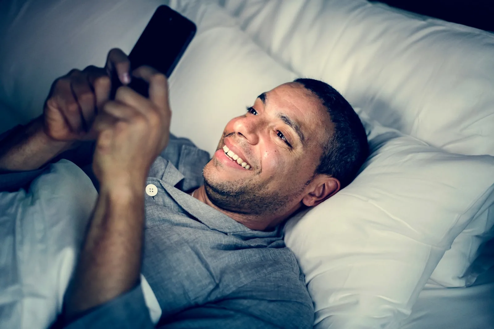 a happy man is lying in bed and using a smartphone