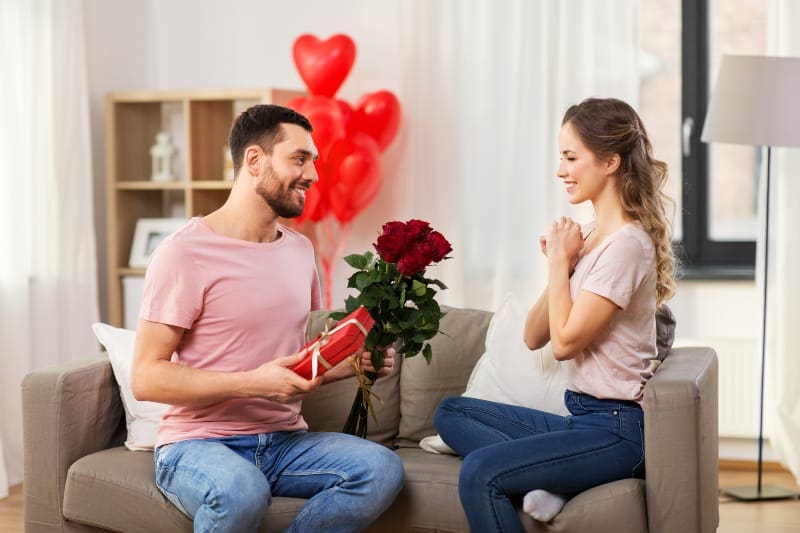 un hombre entrega un regalo y un ramo de rosas rojas a una chica sorprendida