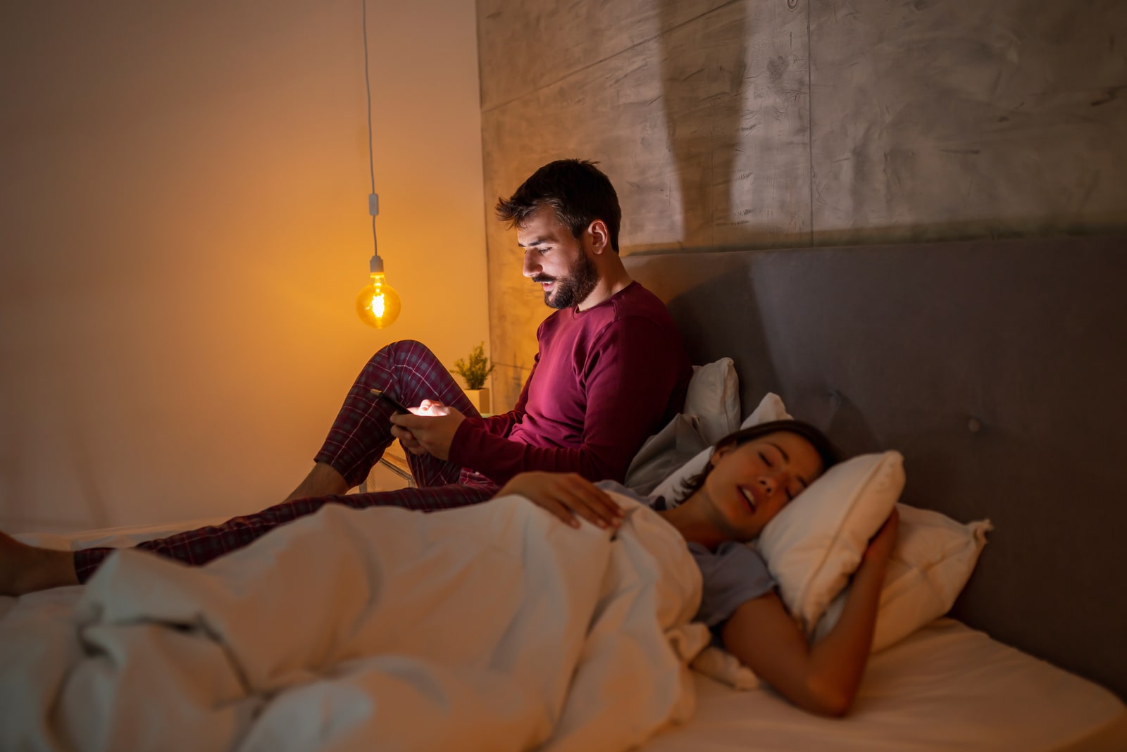 a man in bed uses a smartphone while his girlfriend sleeps