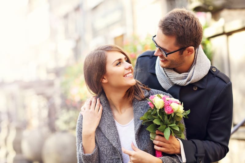 una pareja sonriente abrazándose con un ramo de flores