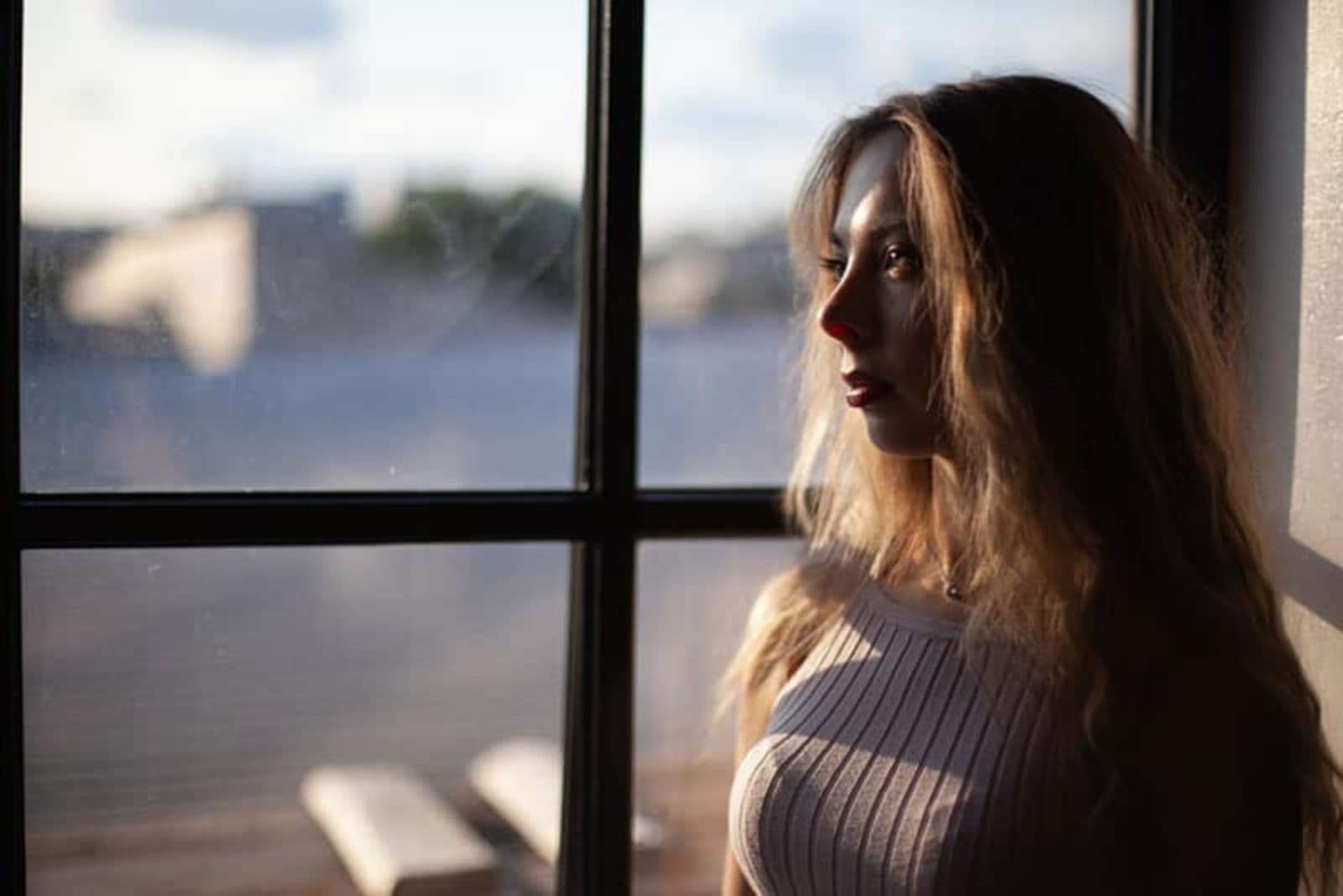a woman with long brown hair stands by the window