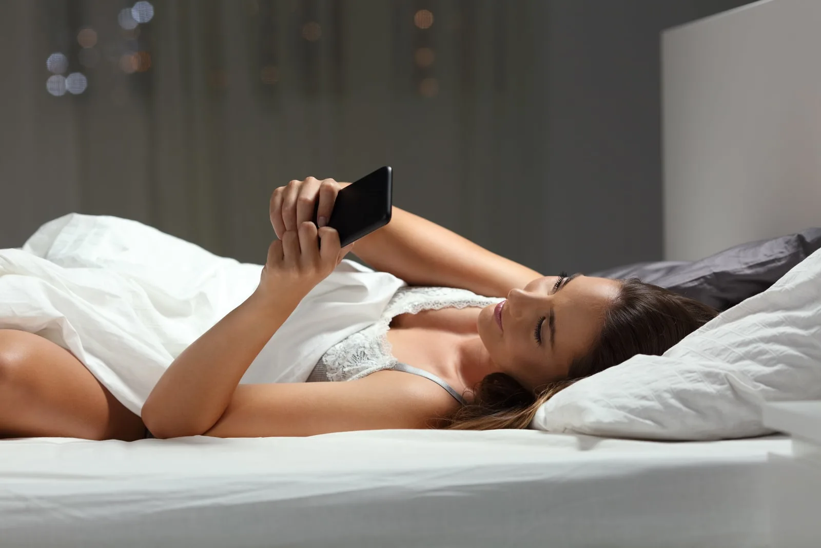 brunette lying in the bedroom bed and using a cell phone