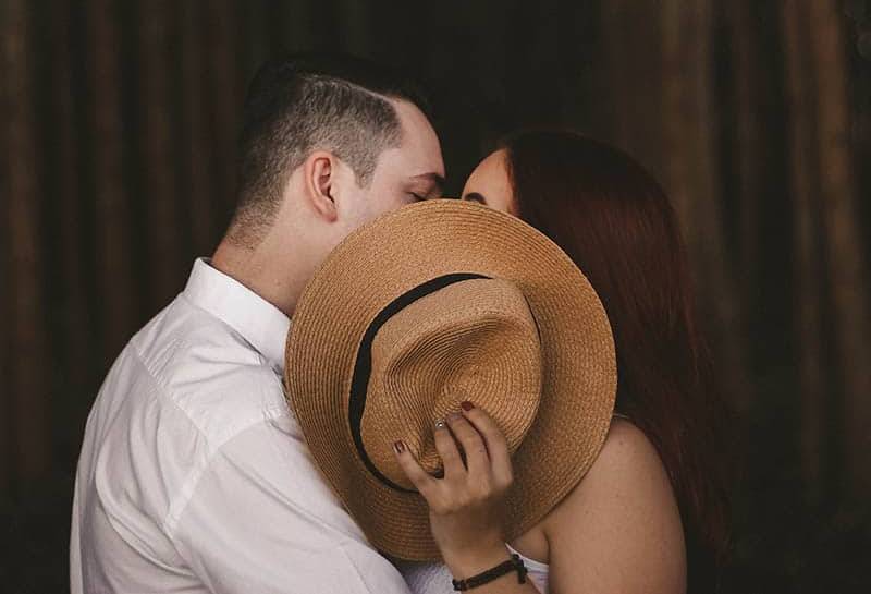 couple kisses while covered mouth with hat