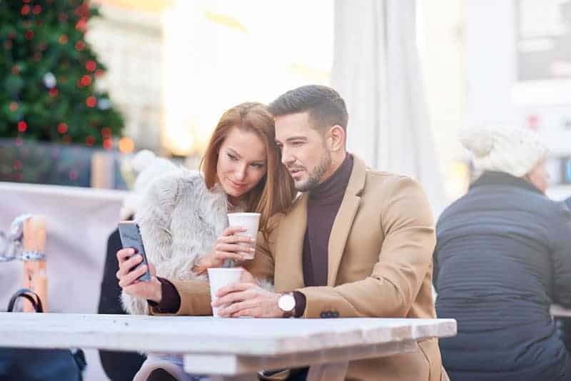 coppia seduta in un caffè all'aperto e guardando lo smartphone