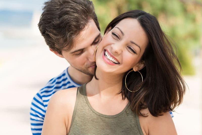 man kissing smiling woman's neck