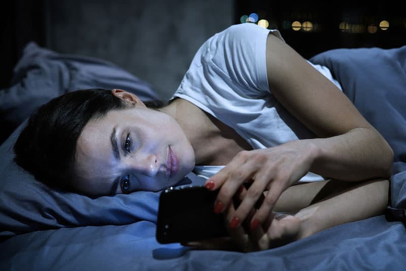 serious woman lying in bed and texting