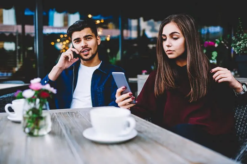 Couple in love spending time in cage together ignoring real communication using gadgets , bored hipster girl chatting online while her boyfriend having mobile conversation addicted to devices