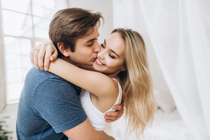 Beautiful loving couple kissing and has fun in their bedroom near the window, a guy holding his beloved beautiful girl in his arms, motion blur