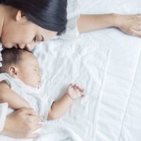 Close up retrato de hermosa joven asiática madre chica besando a su bebé recién nacido dormir en la cama. Cuidado de la salud y el amor médica asia mujer estilo de vida concepto del día de la madre
