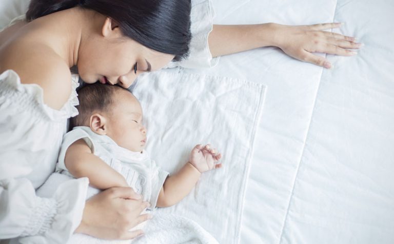 Close up portrait of beautiful young asian mother girl kissing her newborn baby sleep in bed. Healthcare and medical love asia woman lifestyle mother's day concept