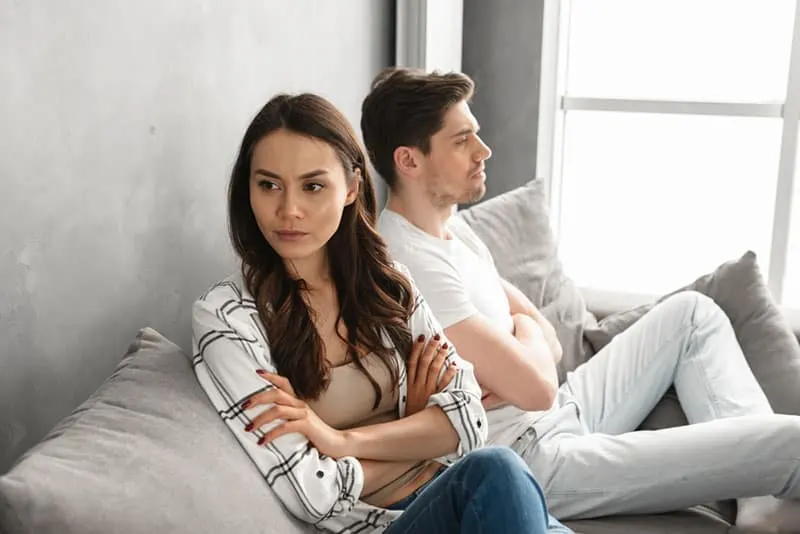 Photo of resentful guy and girl acting like arguing couple and not speaking to each other, while sitting together on couch at home isolated over white background