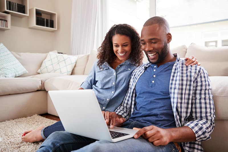 Giovane coppia di colore che usa il computer portatile seduta sul pavimento di casa