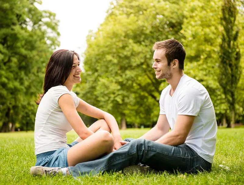 Young happy couple talking together outdoor - sitting on grass