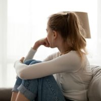 Side view young woman looking away at window sitting on couch at home. Frustrated confused female feels unhappy problem in personal life quarrel break up with boyfriend or unexpected pregnancy concept