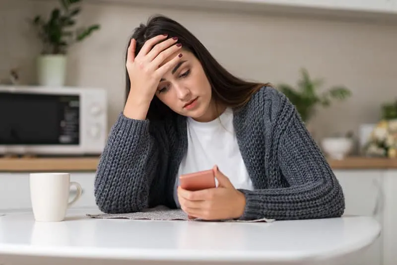 Stressed woman reading something on her cell phone at home