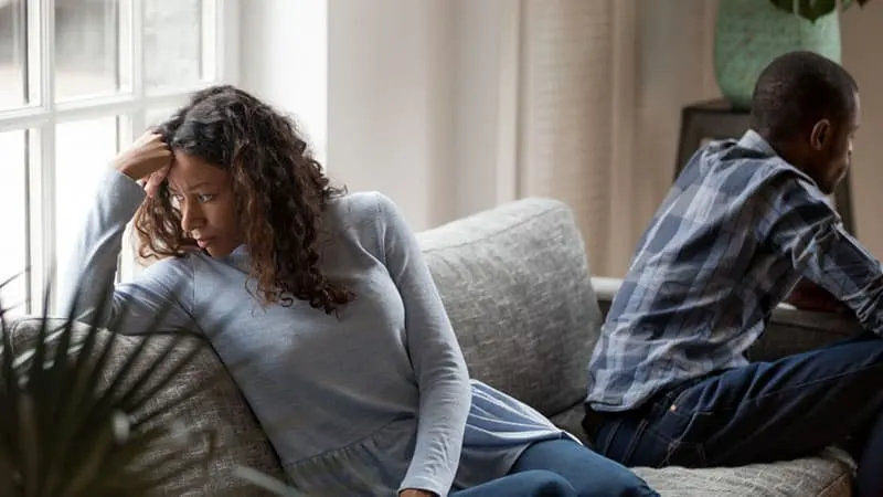 Depressed mixed race couple sit separate on couch having relationships problems, stressed upset black husband and wife avoid talking after fight, sad man and woman think of divorce or breakup