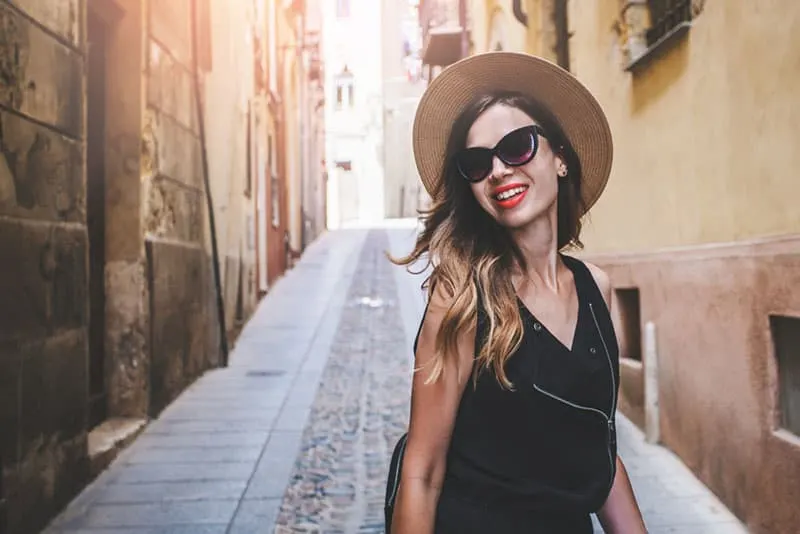 Beautiful hispter tourist girl with a backpack happy smiling walking on the european old town narrow street. Cagliari, Sardinia, Italy. Fashion blogger posing outdoors.