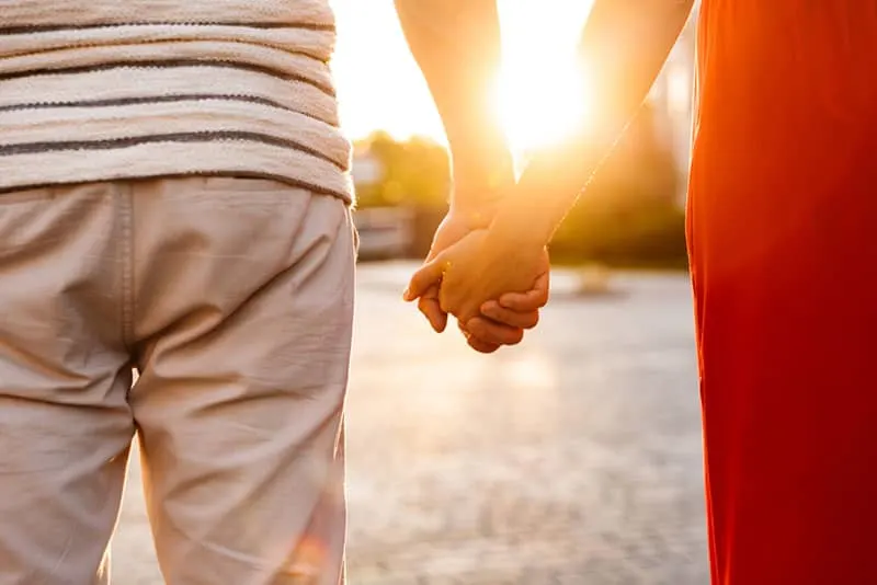 Cropped image of young caucasian couple holding hands together while walking on city street