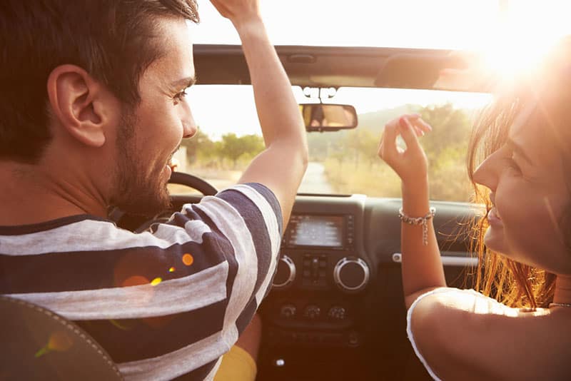 Giovane coppia che guida lungo una strada di campagna in un'auto scoperta