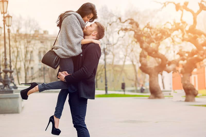 Atraente casal da moda a posar numa rua antiga num outono solarengo. Uma mulher bonita e o seu namorado elegante abraçam-se na rua. Luz solar cremosa de outono.