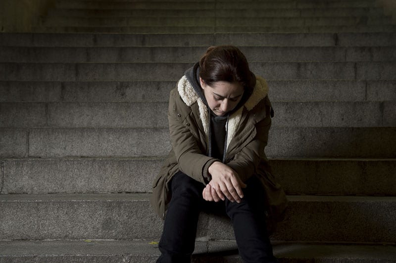 donna triste da sola in strada scala della metropolitana che soffre di depressione guardando malato e impotente seduto solo come vittima femminile di abuso concetto in buio notte urbana grunge sfondo