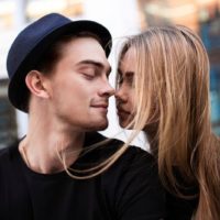 Couple dressed in black looking at each other, the guy wear black hat, a girl flying hair, close-up portrait