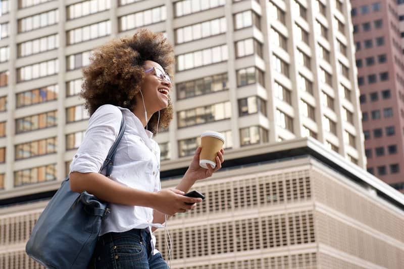 Ritratto laterale di una donna afroamericana sorridente che cammina in città con il cellulare