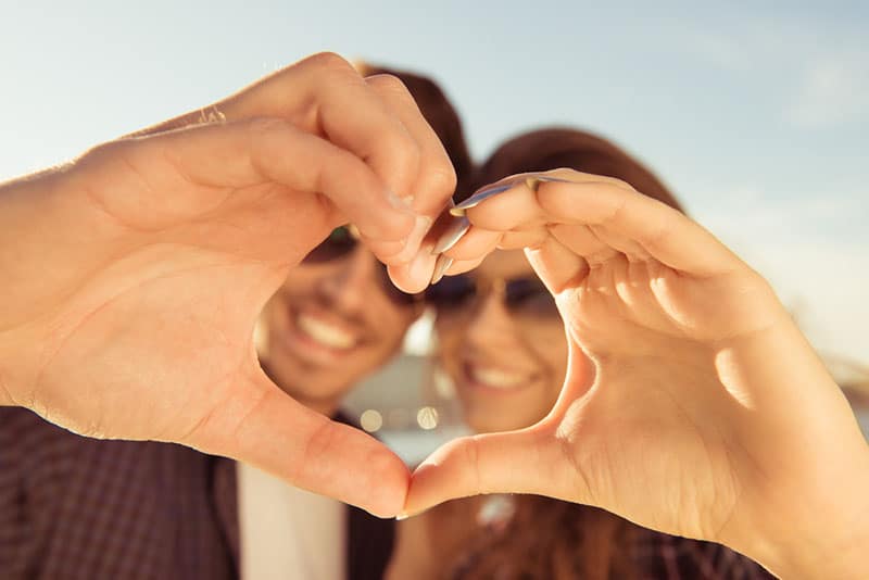 Feliz pareja romántica enamorada gesticulando un corazón con los dedos