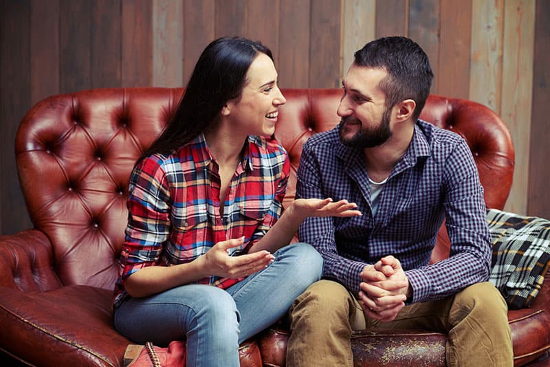 coppia sorridente seduto sul divano e hanno una bella conversazione a casa