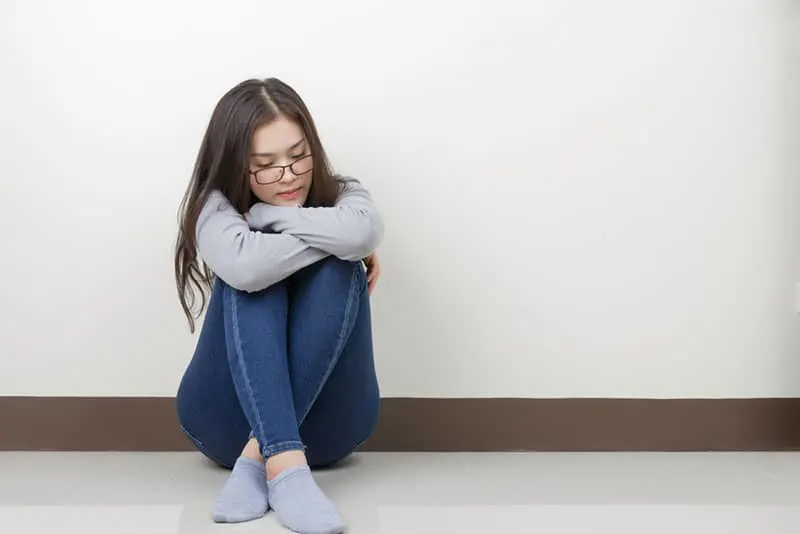 Young Asian woman sitting hugged her knees feel lonely in the room.