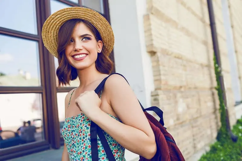 Sunny lifestyle fashion portrait of young stylish hipster woman walking on the street, wearing trendy outfit, straw hat, travel with backpack.