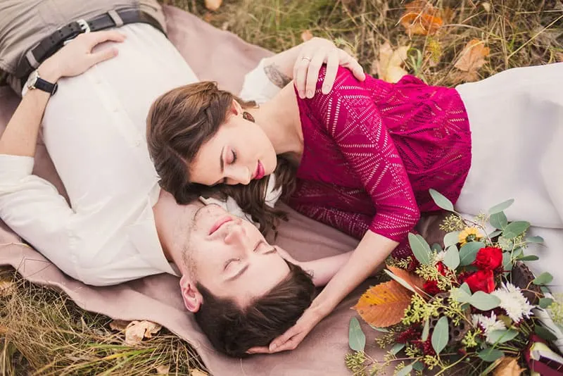 Stylish and romantic caucasian couple lie on the grass and leaves in the beautiful autumn park. Love, relationships, romance, happiness concept.