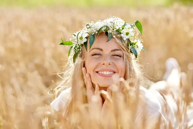 nature, summer holidays, vacation and people concept - face of happy smiling woman or teenage girl n in wreath of flowers on cereal field