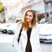 Outdoor lifestyle portrait of amazing glamorous luxury woman posing in city center. Elegant classic clothes in white and black colors. Sensual smile, stunning face. Soft colors.