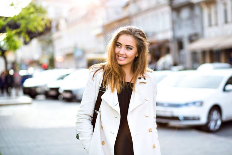 Outdoor lifestyle portrait of amazing glamorous luxury woman posing in city center. Elegant classic clothes in white and black colors. Sensual smile, stunning face. Soft colors.