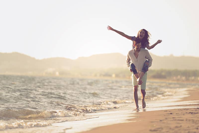 A guy carrying a girl on his back, at the beach, outdoors