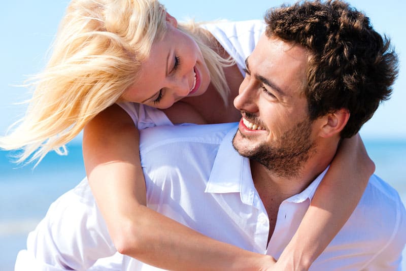 Couple in love - Caucasian man having his woman piggyback on his back under a blue sky on a beach