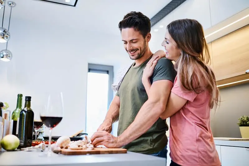 Loving joyful young couple embracing and cooking together, having fun in the kitchen