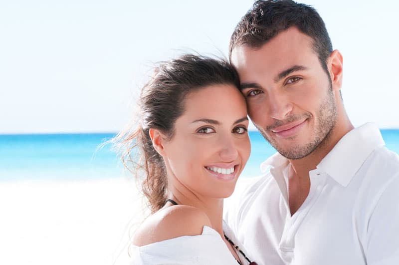 Casal sorridente e feliz a olhar para a câmara na praia de verão