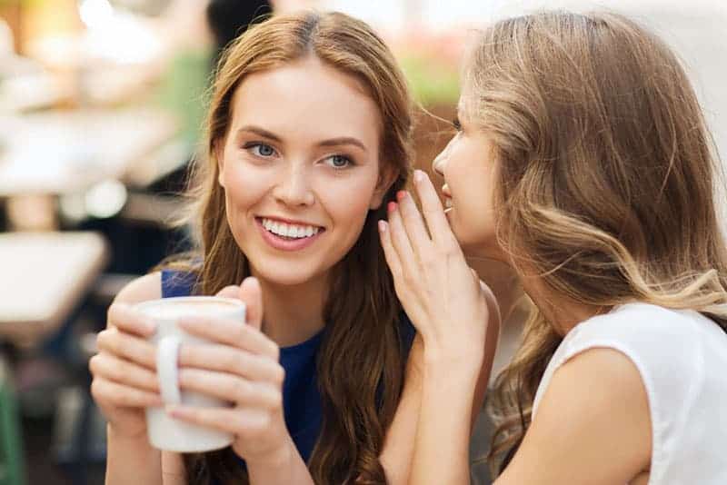smiling young women drinking coffee or tea and gossiping at outdoor cafe